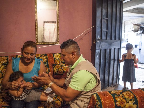 A community health worker (the man in the tan vest) linked to a health center that received USAID Zika support making a home visit to show the mother stimulation exercises to do with her daughter. Photo credit: USAID 2017