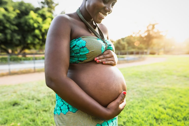 Close up pregnant belly of young African woman in park during sunset time